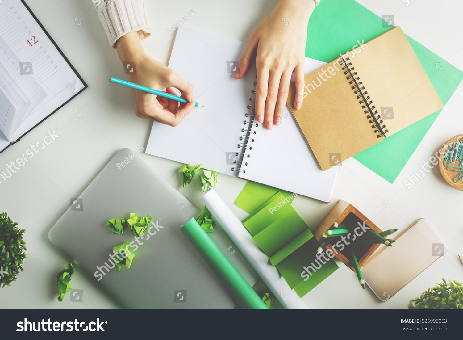stock-photo-woman-with-various-creative-green-items-on-desktop-writing-in-spiral-notepad-top-view-525995053